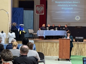 Policjanci siedzący na scenie. Dyrertor szkoły przemawiająca na rozpoczęcie debaty.