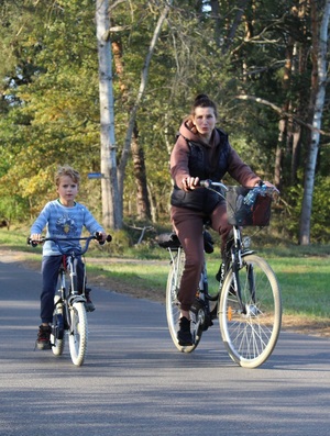 Na rowerze jedzie chłopiec, obok niego na rowerze jedzie kobieta.