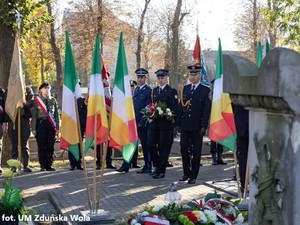 Z kwiatami do złożenia na grobie idą przedstwiciele służb mundurowych.