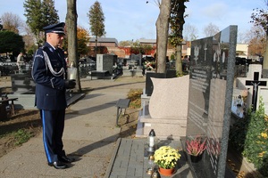 Po lewej stronie, przed tablicą, stoi w galowym umundurowaniu Komendant Powiatowy Policji w Zduńskiej Woli. W ręku trzyma znicz.