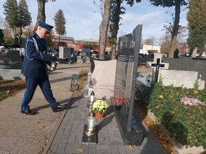 W stronę tablicy idzie w galowym umundurowaniu Komendant Powiatowy Policji w Zduńskiej Woli. W ręku trzyma znicz.