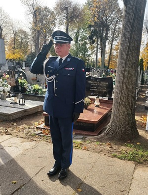 Przed tablicą, stoi w galowym umundurowaniu Komendant Powiatowy Policji w Zduńskiej Woli. Salutuje.