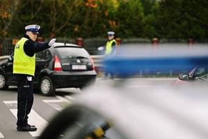 Policjant na skrzyżowaniu kieruje ruchem. W tle cmentarz.