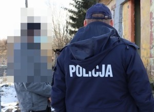 Policjant umundurowany stoi tyłem do zdjęcia, po lewej stronie stoi osoba, rozmawia z policjantem, nie widać twarzy, jest zamazana.