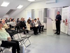 W sali, na krzesełkach siedzą słuchacze konferencji. Na wprost nich stoi policjant, mówi do zgromadzonych.