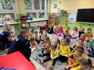 Dzieci siedzą na podłodze, na wprost nich siedzą policjantki, które mówią do dzieci.