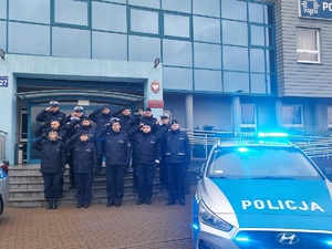 Przed budynkiem komendy stoją radiowozy. Między autami, na schodach, stoją umundurowani policjanci. Salutują.