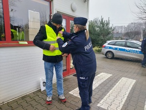 Policjantka zakłada mężczyźnie kamizelkę odblaskową.