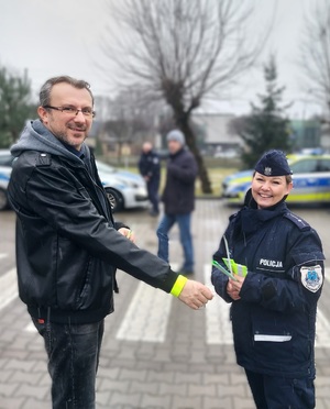 Policjantka daje mężczyźnie na rękę odblaskową opaskę na nadgarstek.