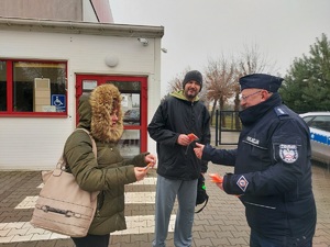 Policjant daje kobiecie i mężczyźnie opaski odblaskowe.