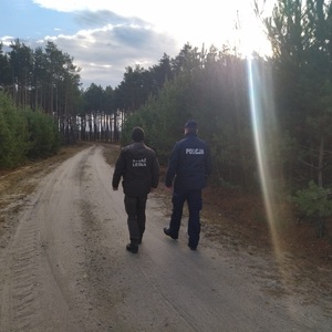 Policjant i strażnik leśny idą drogą w lesie.