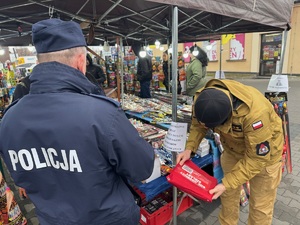 Policjant i strażak kontrolujący stoisko z fajerwerkami.