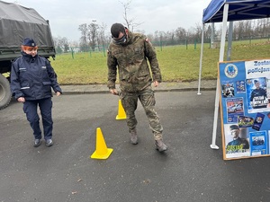 Żołnierz ma założone na oczy alkogogle i pokonuje drogę miedzy pachołkami, obok niego idzie policjantka.