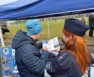 Policjantka pokazuje mężczyźnie odwróconego do zdjęcia tyłem, ulotkę &quot;Zostań policjantem&quot;.