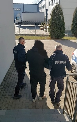 Dwóch policjantów sprowadza na dół po schodach zatrzymanego.