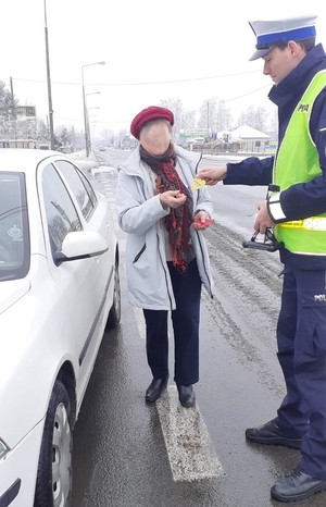 Policjant daje serduszko zapachowe kobiecie, która stoi obok auta.