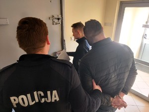 Zatrzymany jest wprowadzany przez dwóch umundurowanych policjantów do celi.