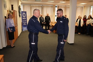 Aula w komendzie, dowódca uroczystości składa meldunek komendantowi. W tle stoją inne osoby.