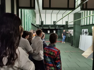 Instruktor wyszkolenia strzeleckiego, pokazuje dzieciom na strzelnicy tarcze oraz całe pomieszczenie.