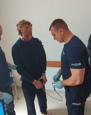 Policjant zakłada zatrzymanemu kajdanki.