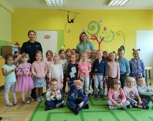 Grupowe zdjęcie przedszkolaków i policjantki w sali.