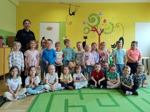 Grupowe zdjęcie przedszkolaków i policjantki w sali.
