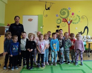 Grupowe zdjęcie przedszkolaków i policjantki w sali.