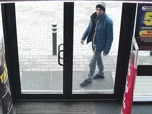 Do przeszklonych drzwi dochodzi mężczyzna, ubrany w kurtkę i czapkę. Wchodzi do sklepu.