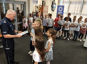 Aula komendy. Komendant wręcza grupie dzieci dyplom.