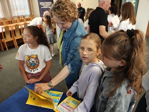 Aula komendy. Uczestnicy oglądają prace plastyczne rozłożone na stoliku.
