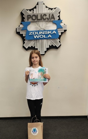 Dziewczynka pozuje do zdjęcia ze swoją pracą plastyczną.