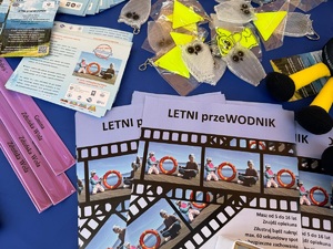 Na stoliku leżą odblaski i różne gadżety policyjne, a także ulotki dotyczące bezpieczeństwa nad wodą.