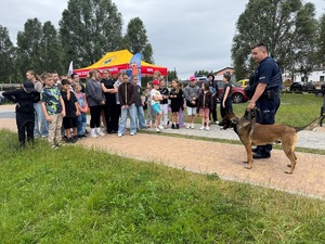 Policjant z psem stoją na wprost grupy młodzieży. Policjant do nich mówi.