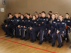 Uczniowie w umundurowaniu szkolnym, siedzą na krzesełkach.