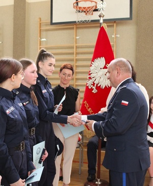 Komendant wręcza uczennicy pagon, ściska jej rękę gratulując.