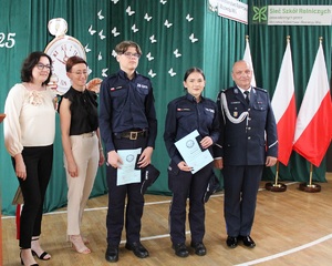 Do zdjęcia pozuje dwoje uczniów w mundurach, policjant i dwie nauczycielki.