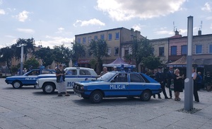 Stoją zaparkowane na placu stare, zabytkowe samochody milicyjne.