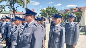 Policjanci stoją w rzędach, są w pełnym umundurowaniu.