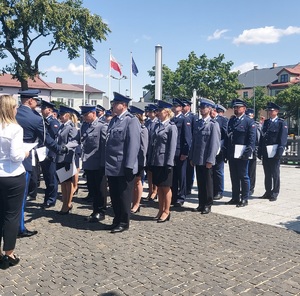 Policjanci stoją w rzędach, mają wręczane akty mianowania na wyższe stopnie policyjne.