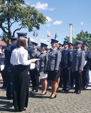 Policjanci stoją w rzędach, mają wręczane akty mianowania na wyższe stopnie policyjne.