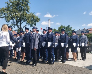 Policjanci stoją w rzędach, mają wręczane akty mianowania na wyższe stopnie policyjne.