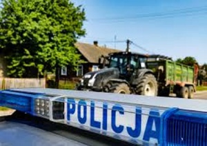 Światła błyskowe policyjne radiowozu, na tle traktora z przyczepą.