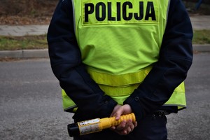 Umundurowany policjant stoi tyłem do zdjęcia. Trzyma w rękach urządzenie do kontroli stanu trzeźwości.