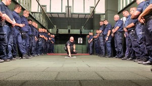 Strzelnica. Instruktor tłumaczy zebranym, pokazuje na tarczę którą położył na podłodze.