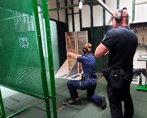 Policjant strzela klęcząc na jedno kolano. Obok niego stoją instruktorzy.