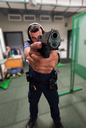 Policjant ma broń, celuje, lufa jest skierowana w stronę zdjęcia.