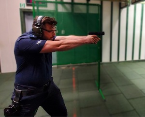 Policjant mierzy pistoletem do tarczy. Widać go z boku.
