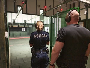 Policjantka stoi przygotowana do strzelania, za nią stoi instruktor.