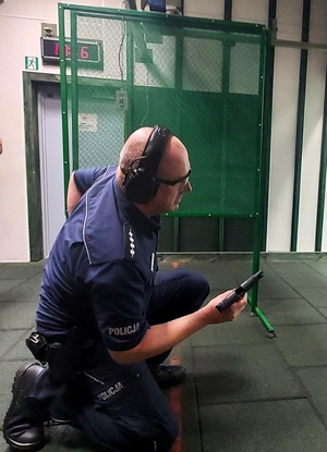 Policjant klęczy w czasie strzelania, zmienia magazynek w pistolecie.