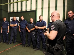 Policjanci stoja w szeregu, przed nimi jest instruktor, tłumaczy im.